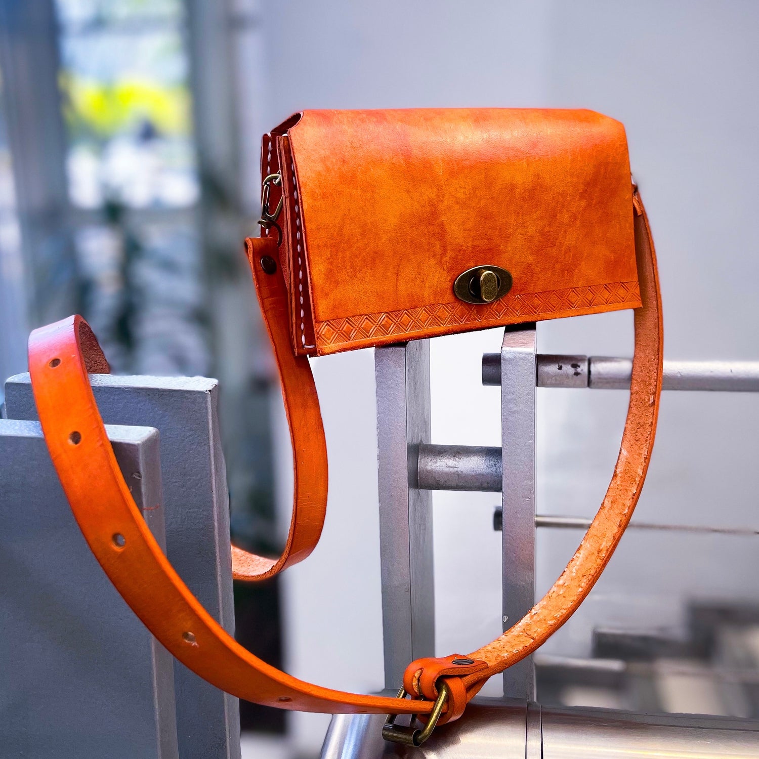 Orange leather bag with a strap on a metal stand against a blurred indoor background