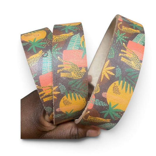A patterned belt with a tropical print, held in a hand against a plain white background.