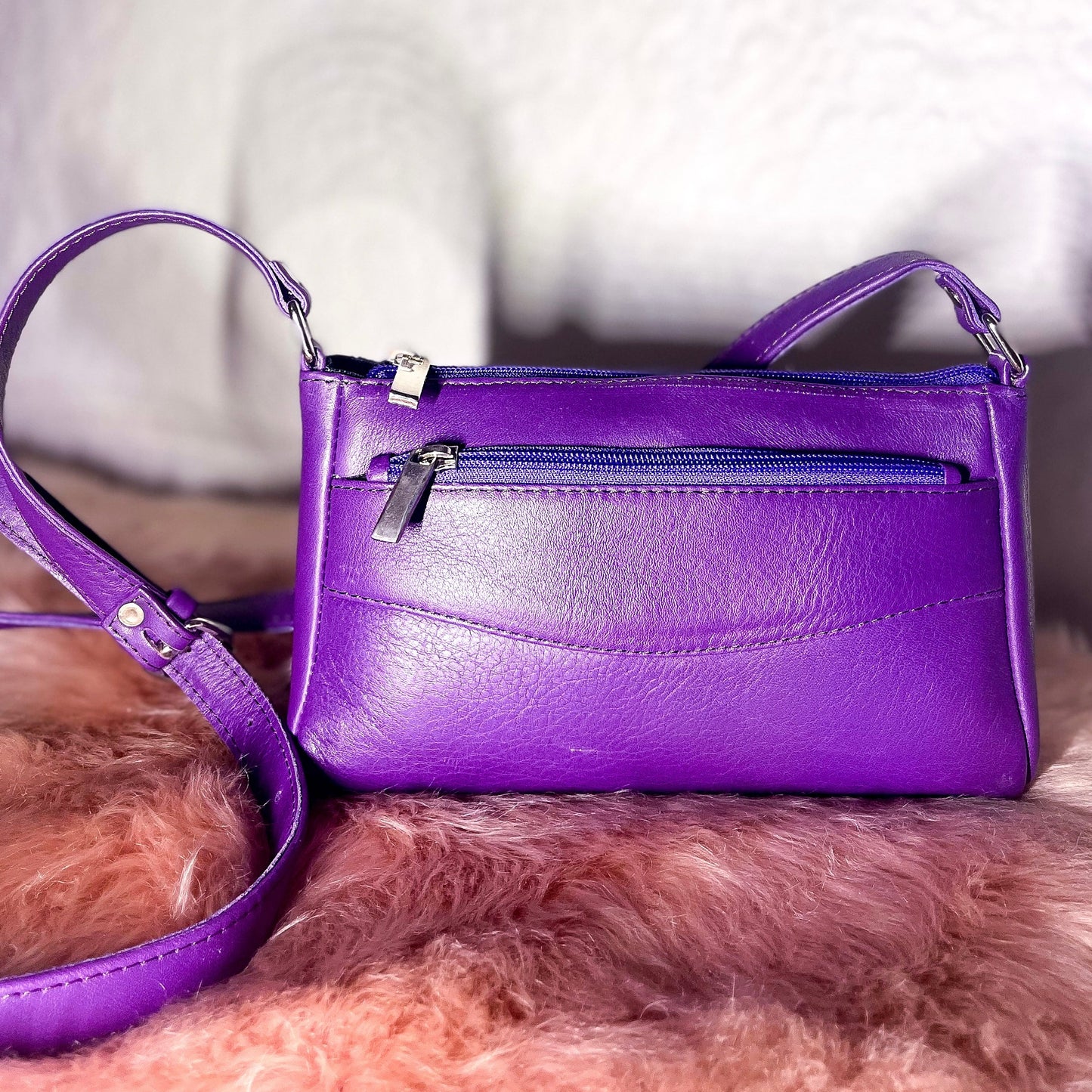 Purple handbag with a matching strap on a fluffy pink surface