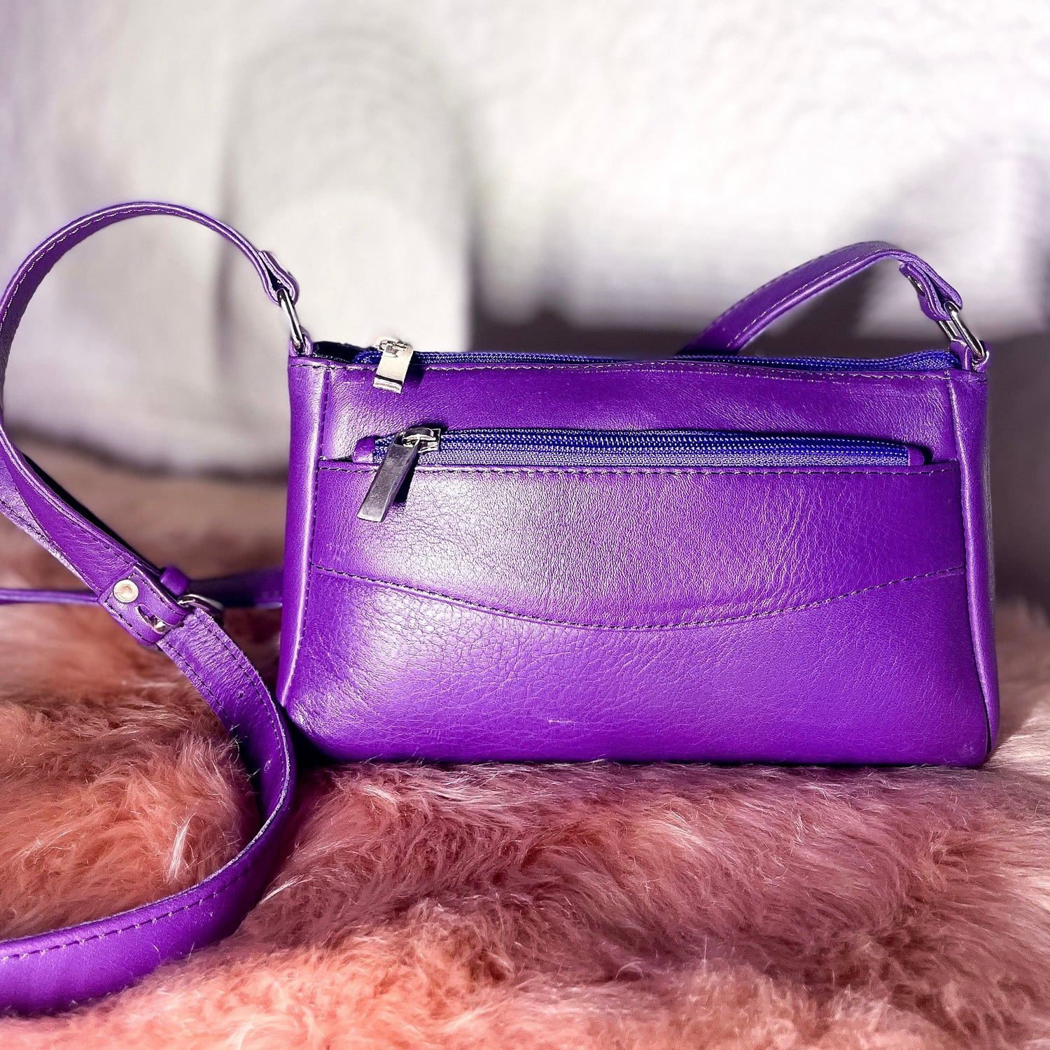 Purple handbag with a matching strap on a fluffy pink surface