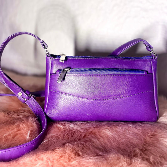 Purple handbag with a matching strap on a fluffy pink surface