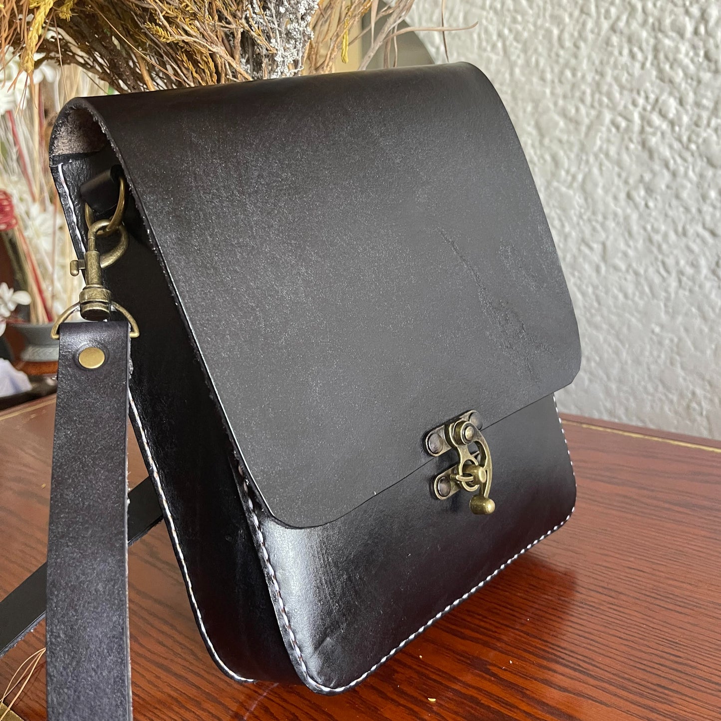 black genuine leather hand- stitched cross body on a table behind flowers