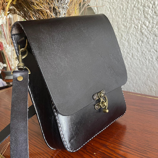 black genuine leather hand- stitched cross body on a table behind flowers