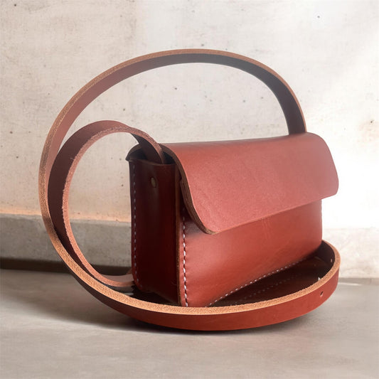 Brown leather handbag with a strap on a light background