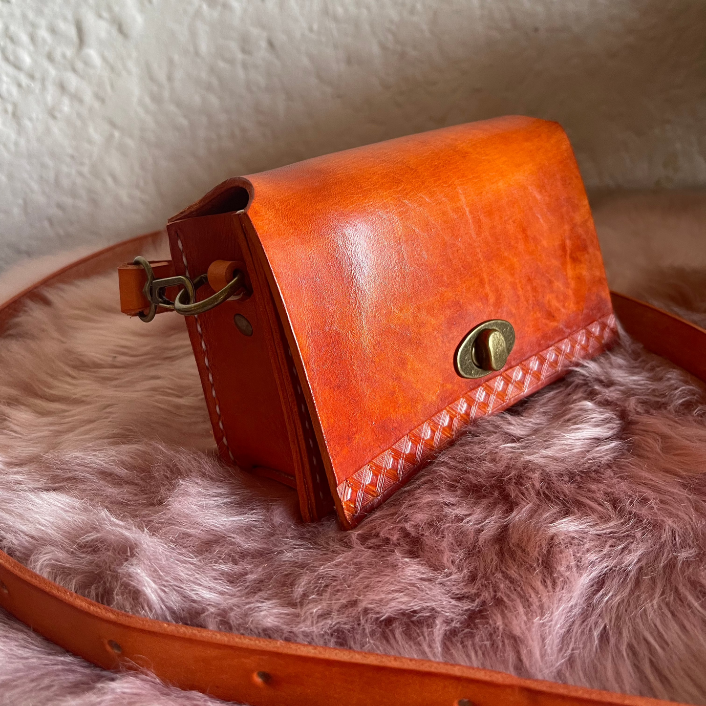A small orange brown cow leather sling bag with a faux fur lining, placed on a faux fur surface.