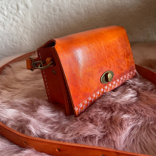 A small orange brown cow leather sling bag with a faux fur lining, placed on a faux fur surface.