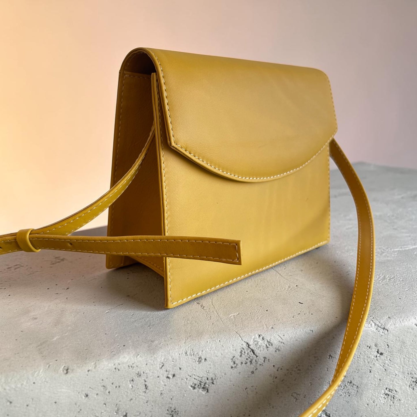 Yellow leather handbag on a textured surface with a soft pink background