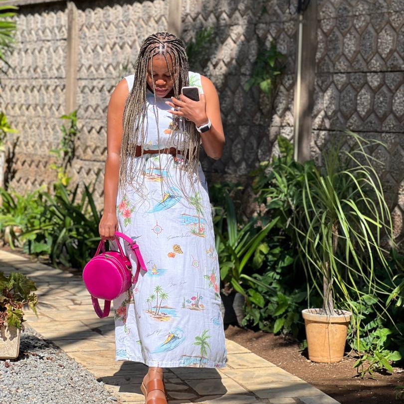 Woman in a floral dress with a pink bag walking outdoors.
