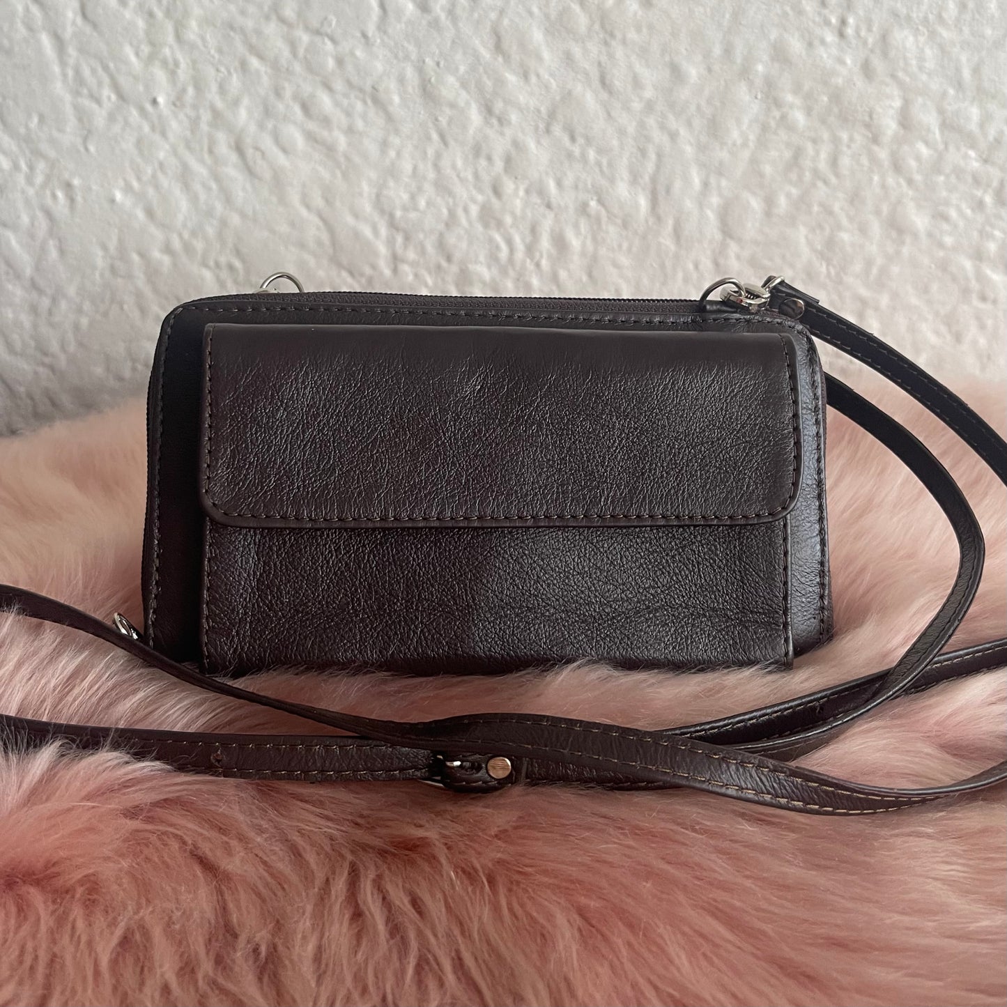 Black leather crossbody bag on a pink fur surface with a white wall background