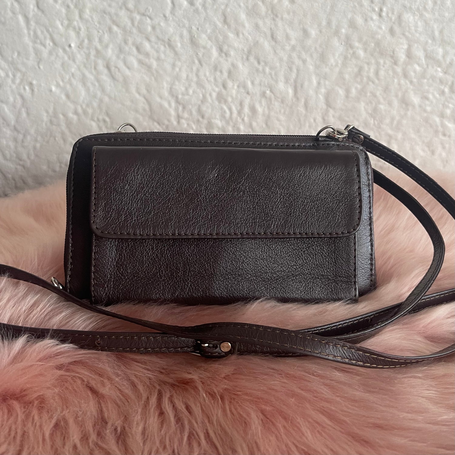 Black leather crossbody bag on a pink fur surface with a white wall background