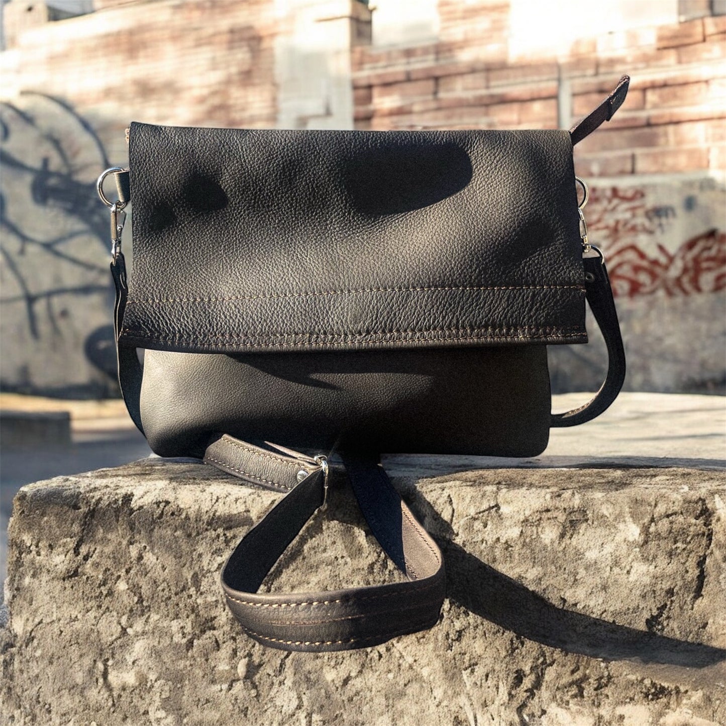 Black leather handbag on a stone ledge with graffiti in the background
