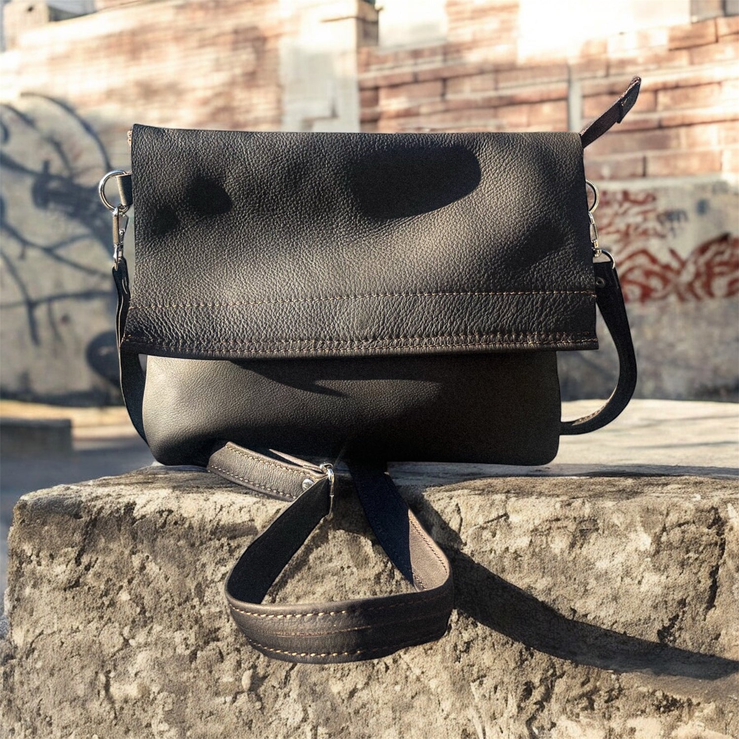 Black leather handbag on a stone ledge with graffiti in the background