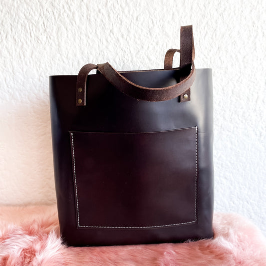 Brown leather tote bag on a pink fur surface with a white wall background