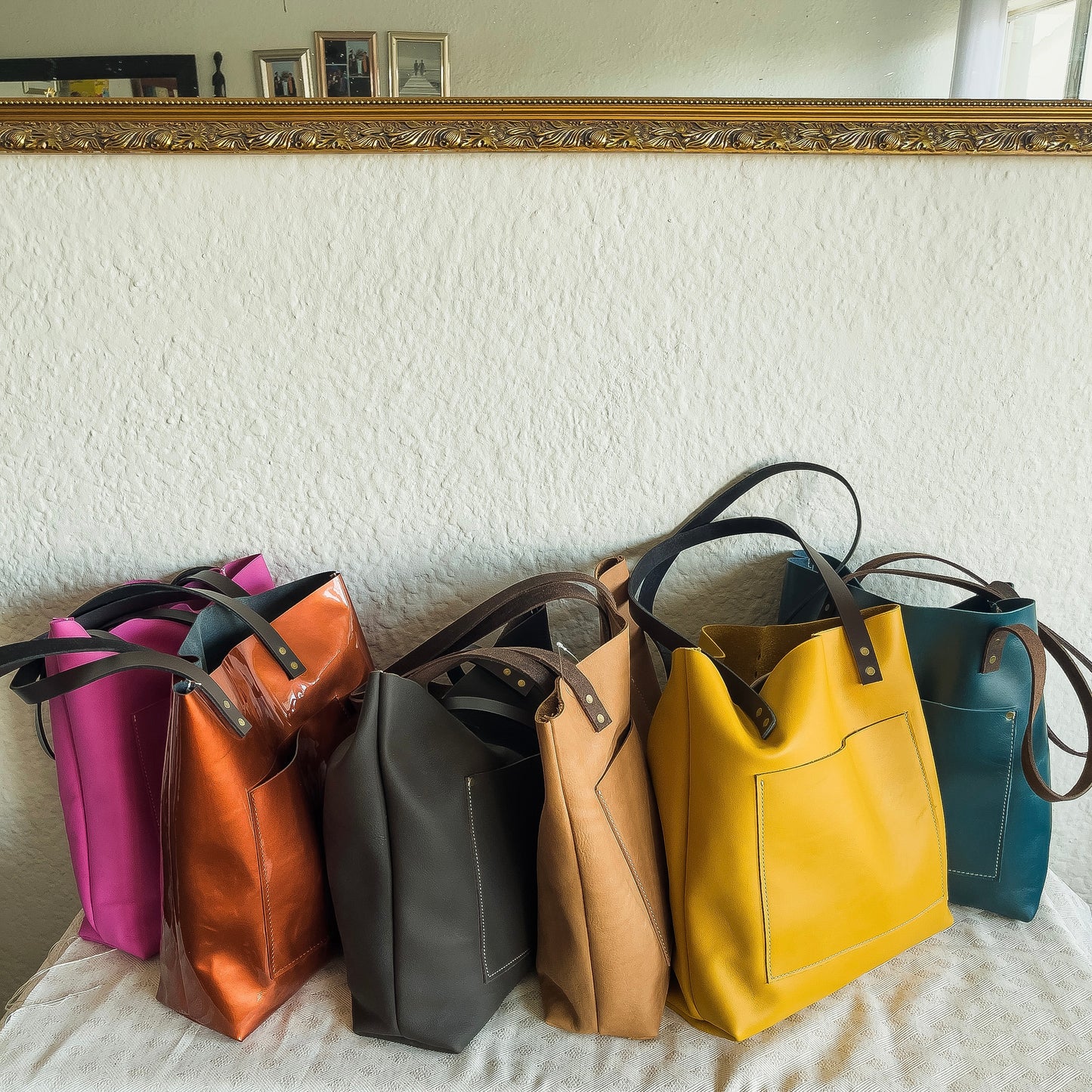 Five leather handbags in various colors arranged on a surface with a decorative mirror in the background.