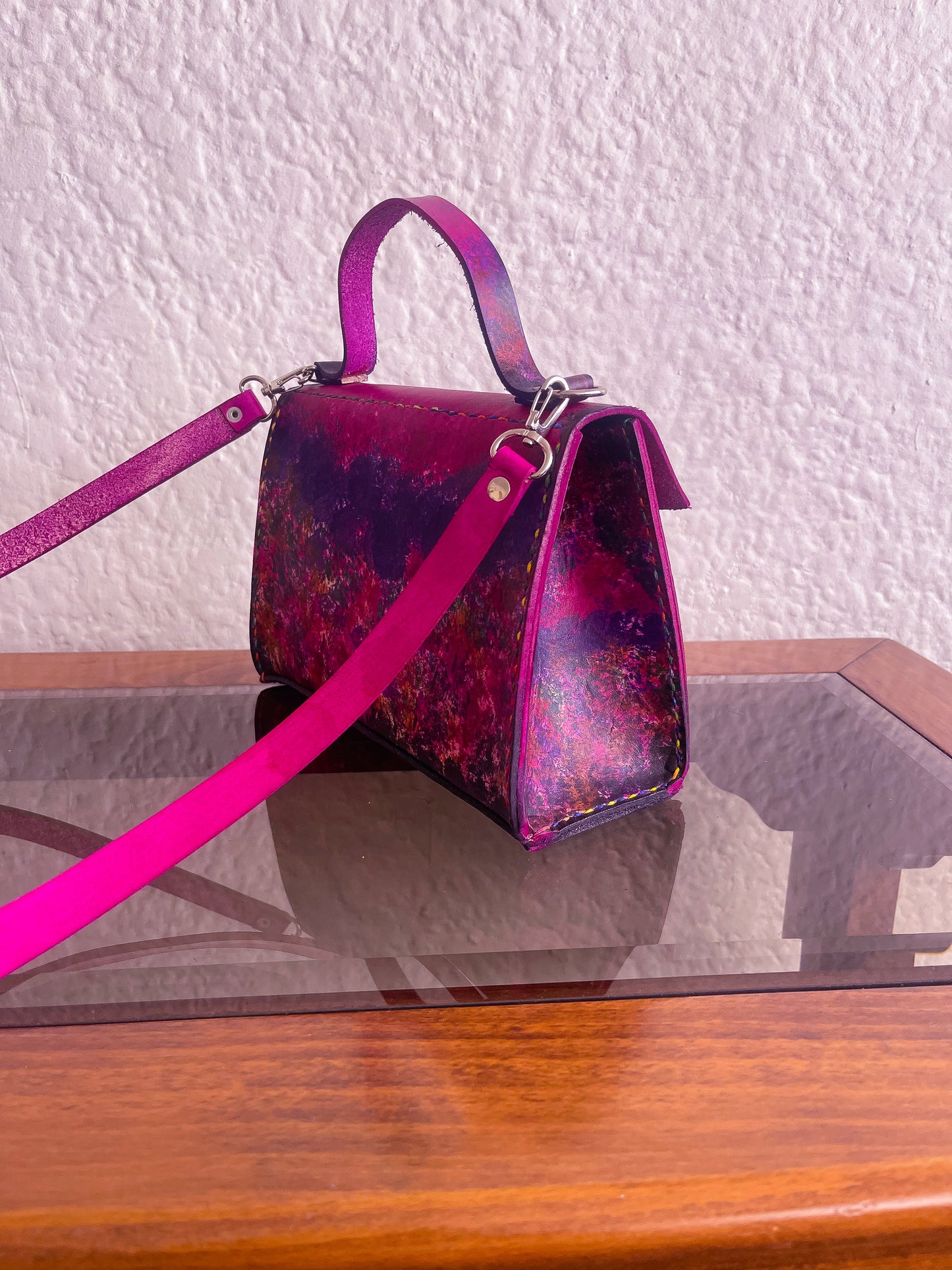 Purple handbag with pink strap on a reflective surface
