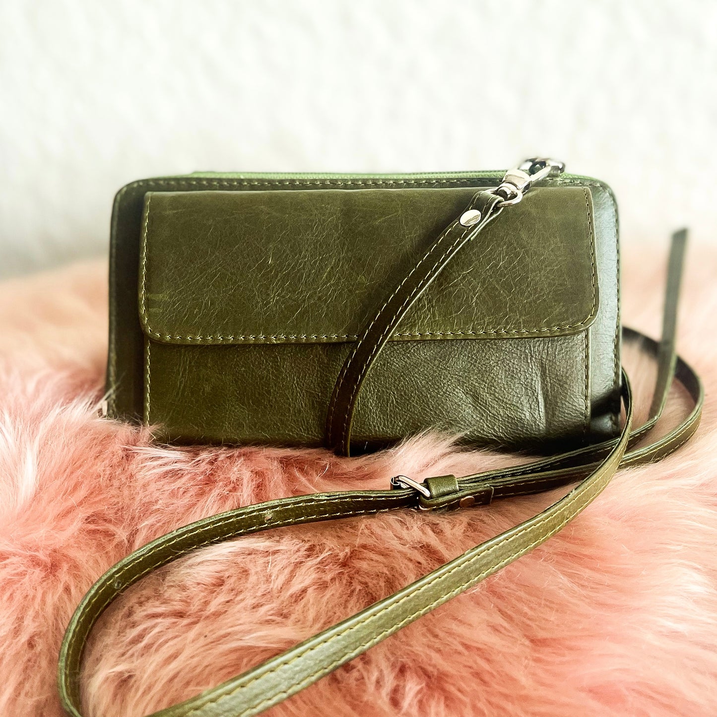 Green leather clutch bag with a strap on a pink fluffy surface