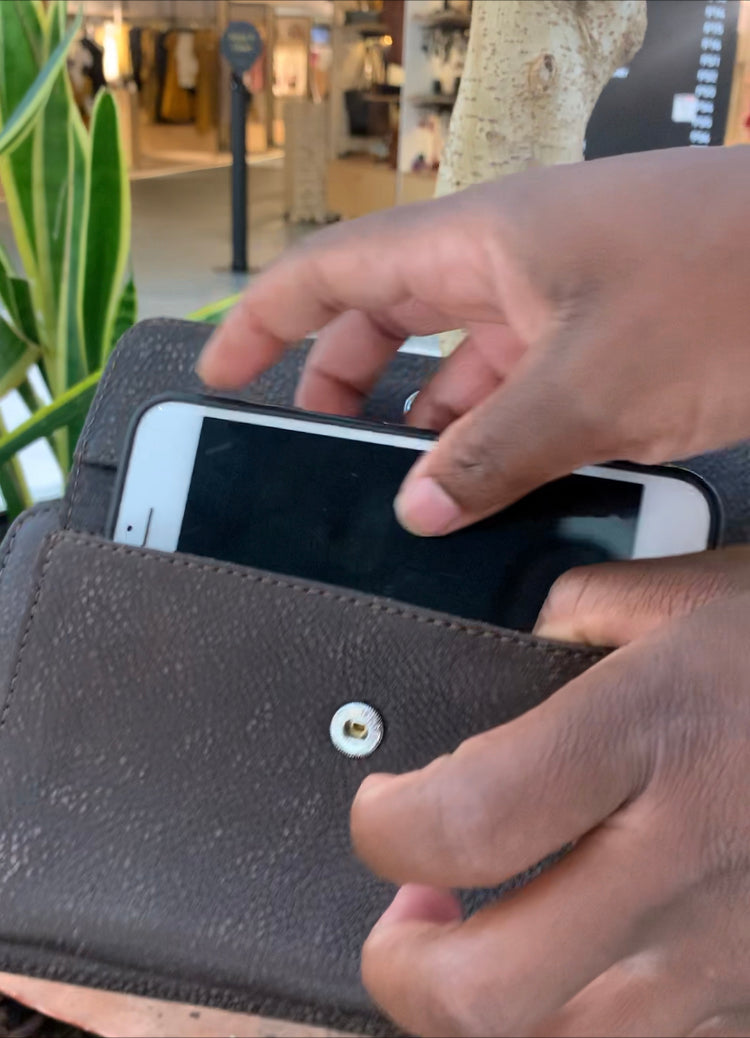 Person using a smartphone in a leather wallet with a blurred indoor background