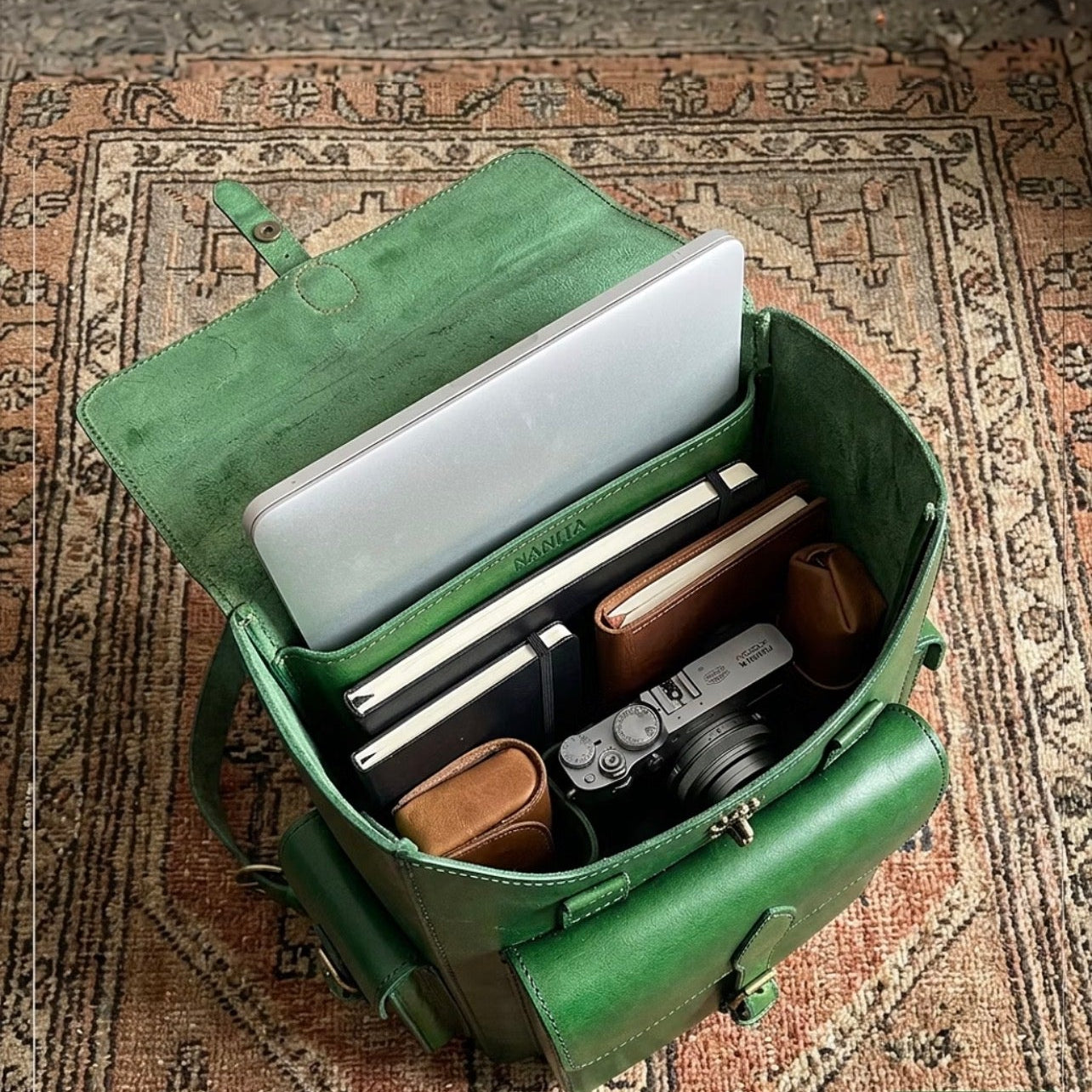 Green leather bag with laptop and items on a patterned rug