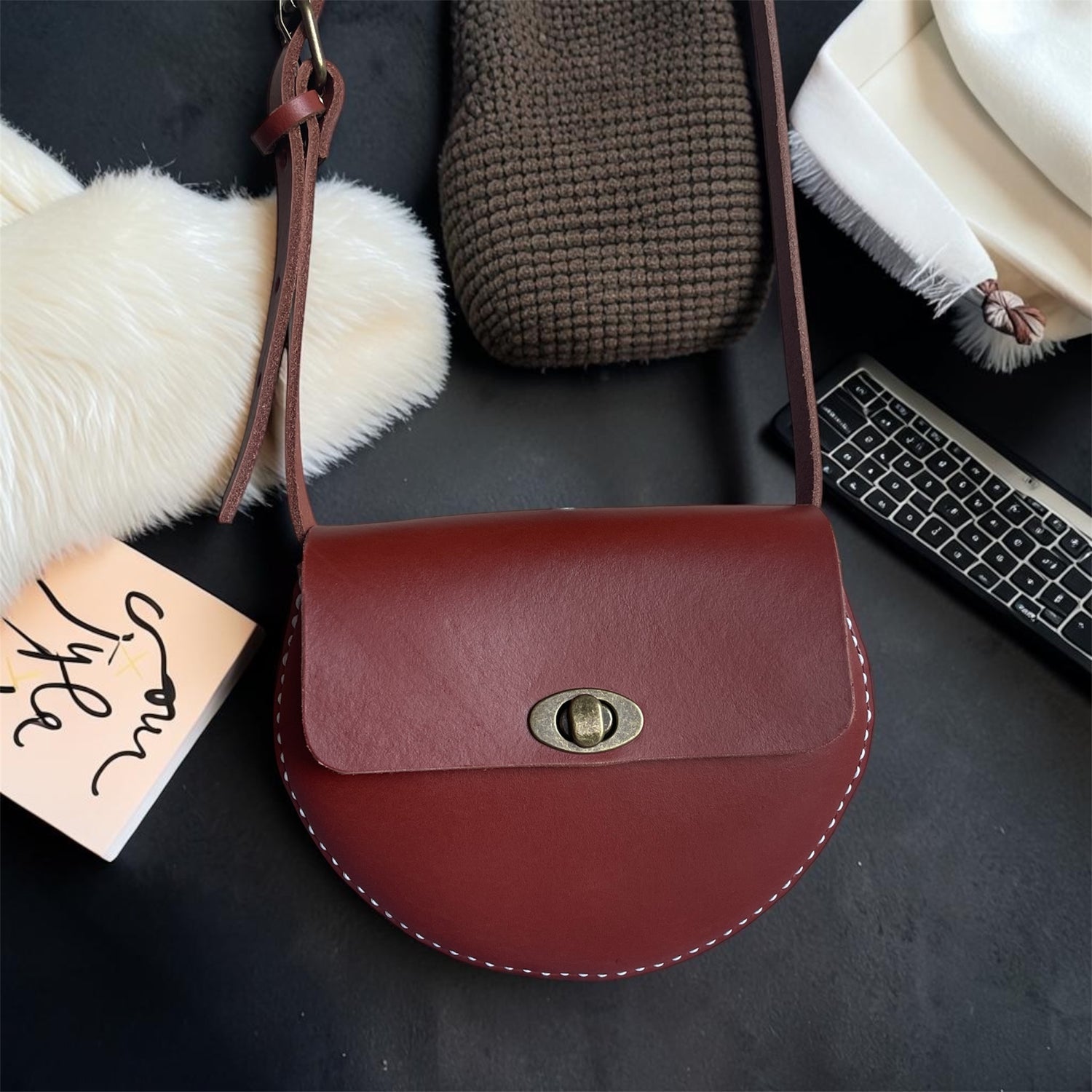 Red handbag with a gold clasp on a dark surface with a keyboard and textured items.