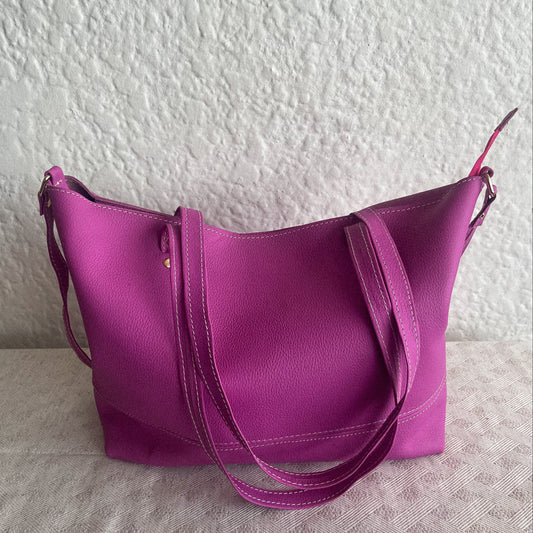 Purple handbag on a textured surface with a white wall background