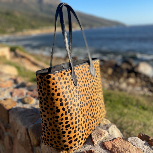 Leopard print tote handbag on a stone wall with a scenic background of water and mountains.