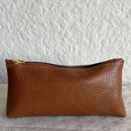 Brown leather pouch with a gold zipper on a textured white background