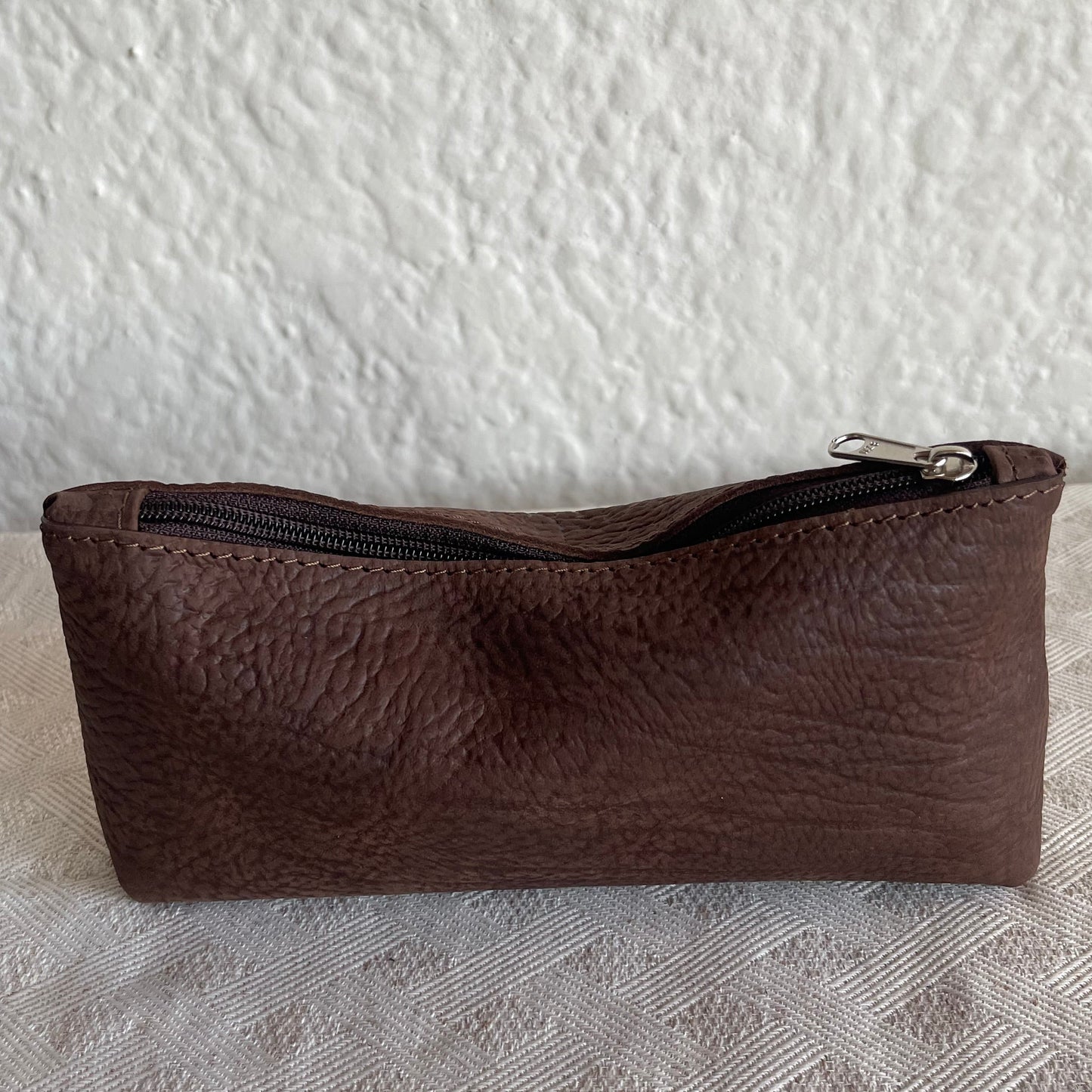 Brown leather pouch with a zipper on a textured white background