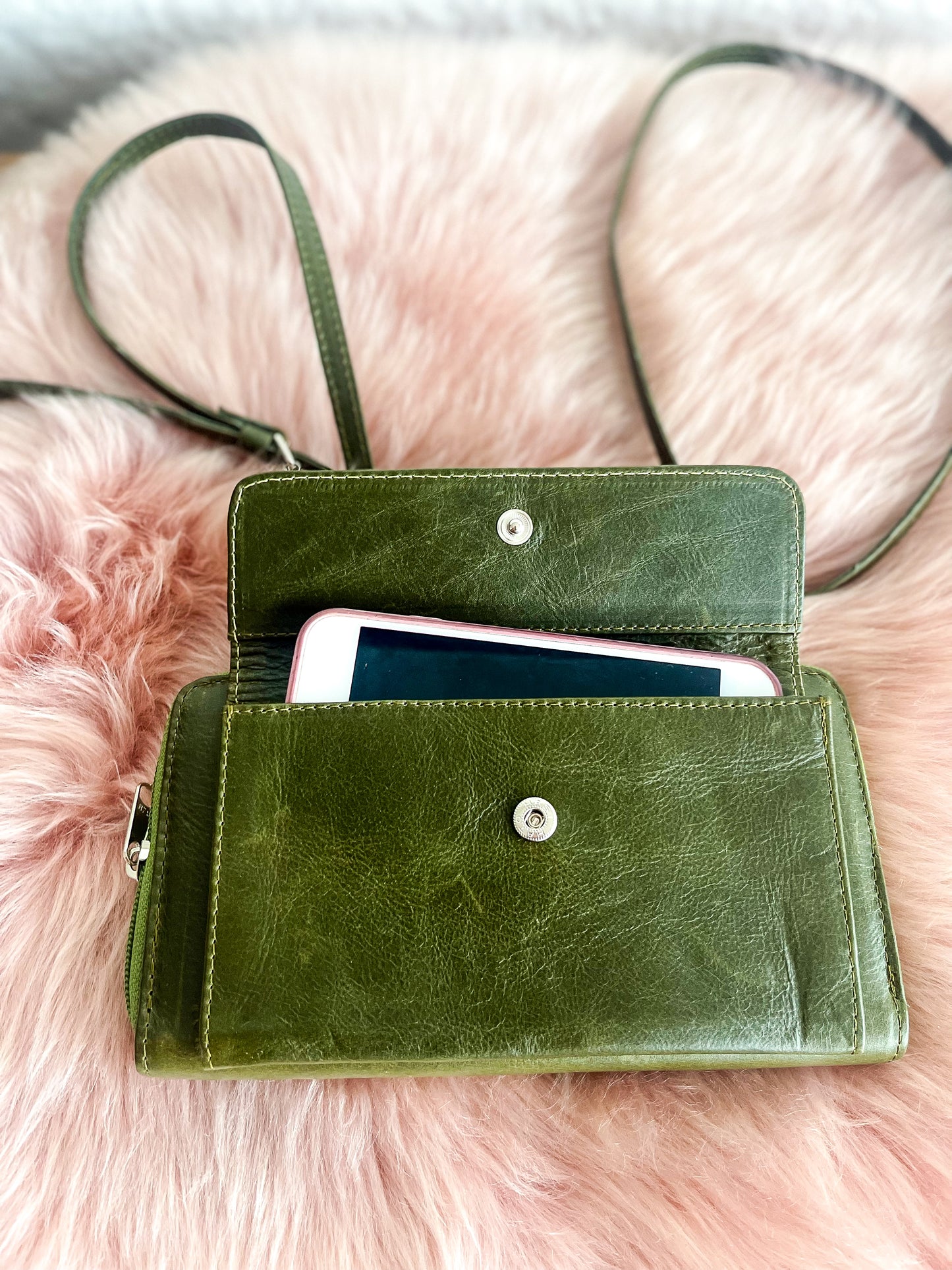 Green leather wallet with a phone inside on a pink fur background