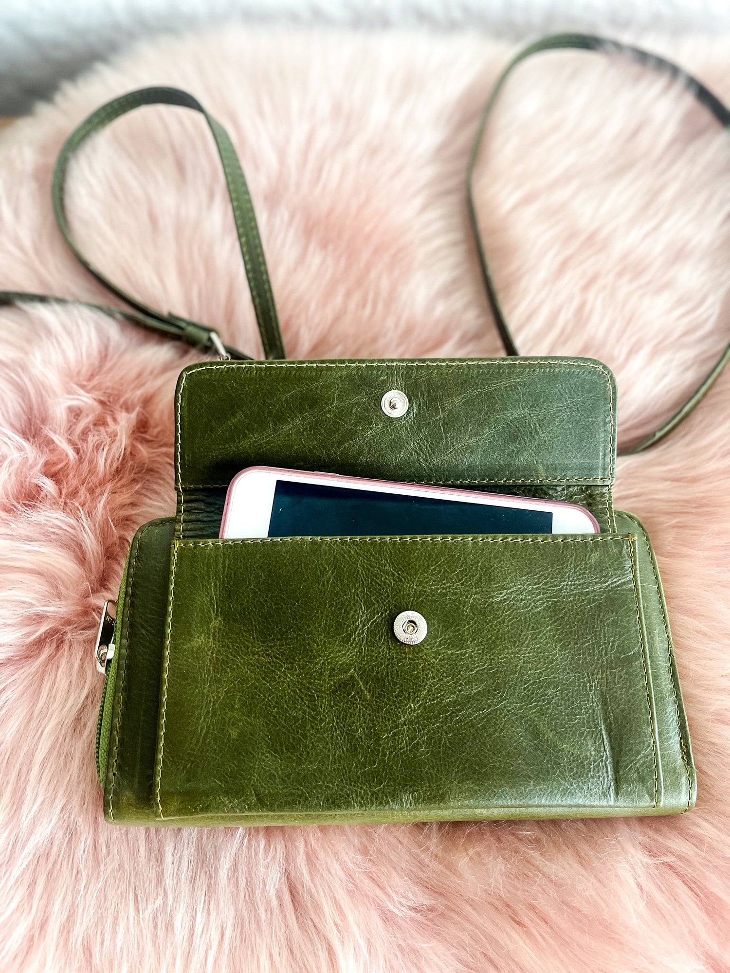 Green leather wallet with a phone inside on a pink fur background
