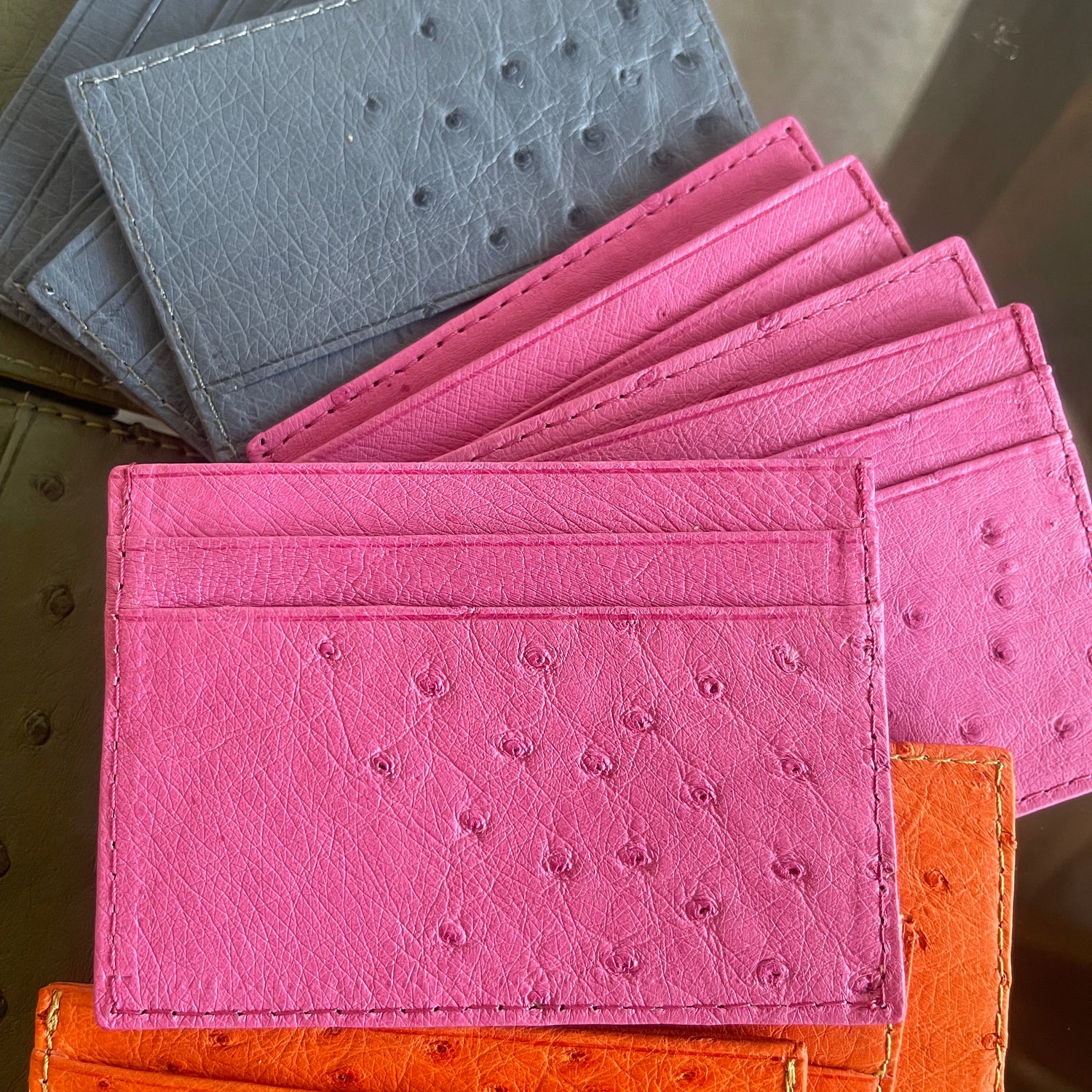 Set of pink, gray, and orange leather card holders on a textured surface.