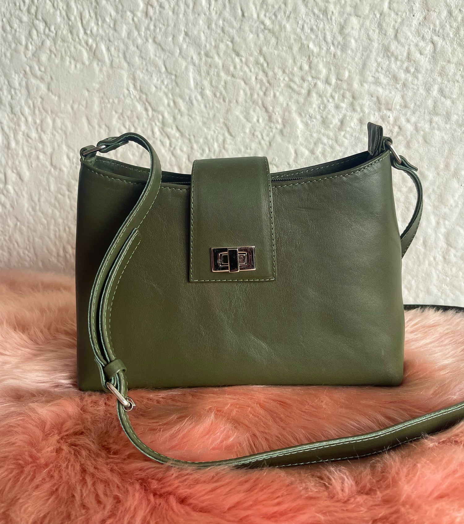 Green leather handbag on a pink fur surface with a white wall background