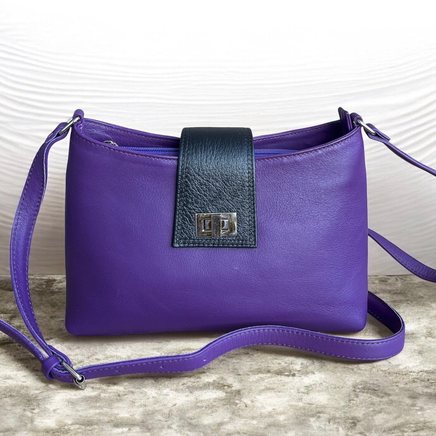 Purple handbag with a black strap on a textured surface