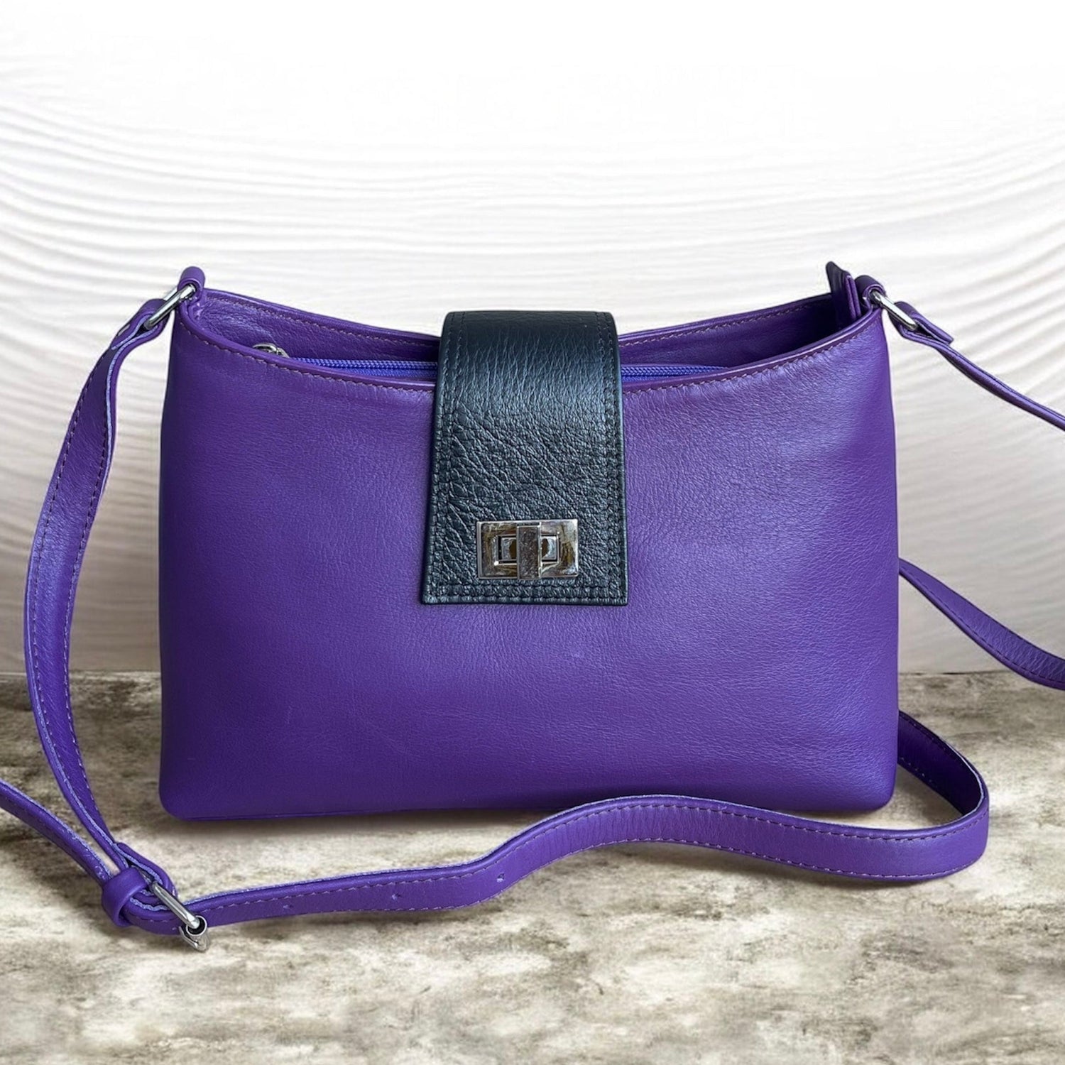 Purple handbag with a black strap on a textured surface
