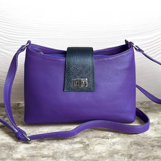 Purple handbag with a black strap on a textured surface