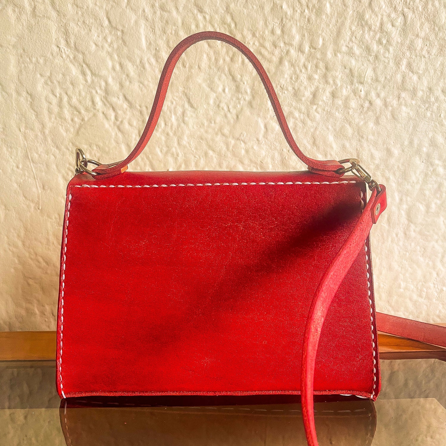 Red handbag on a reflective surface with a textured wall background