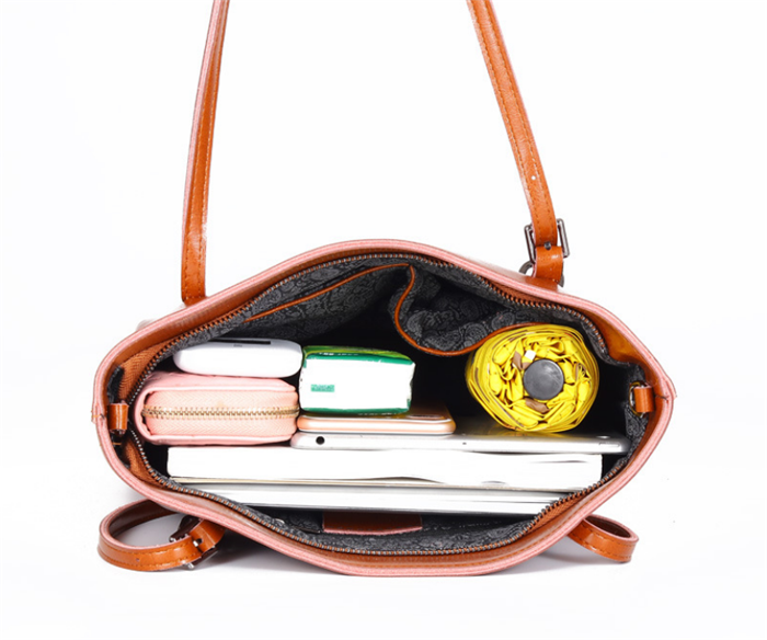 Open brown handbag with items including a yellow ball, books, and a pink item on a white background