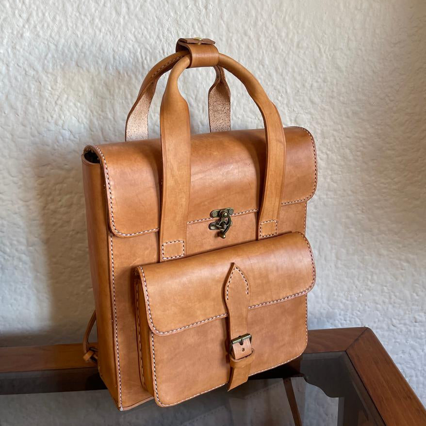 Brown leather backpack on a reflective surface with a textured white wall background