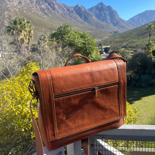 Brown leather bag on a chair with a scenic background of mountains and trees.
