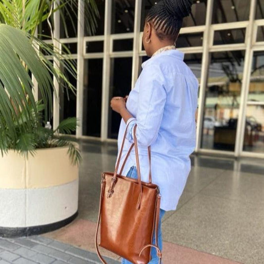 A person is standing with their back to the camera, holding a brown leather tote bag.