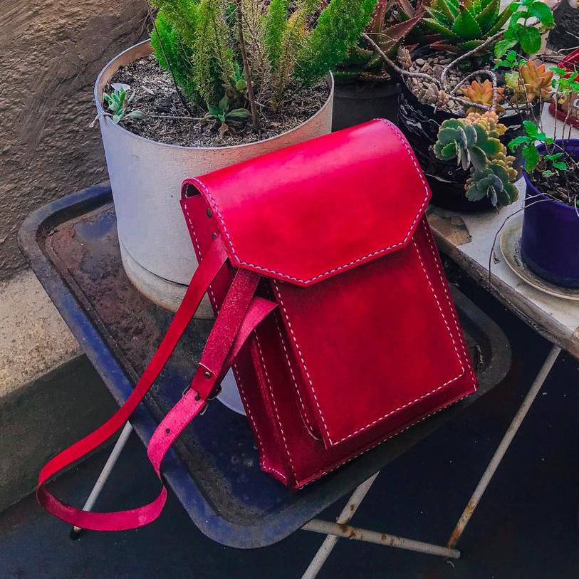 red hand-stitched genuine leather man bag in a flower garden